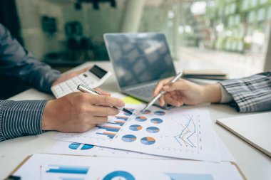 Profesyonel iş ortaklarından oluşan bir ekip elinde kalem tutarak mali grafik belgesini işaret ediyor, analiz ve strateji danışmanlığını hesaplıyor. Toplantı, ofiste beyin fırtınası, takım çalışması konsepti..