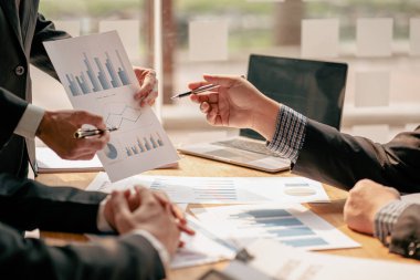 Profesyonel iş ortaklarından oluşan bir ekip elinde kalem tutarak mali grafik belgesini işaret ediyor, analiz ve strateji danışmanlığını hesaplıyor. Toplantı, ofiste beyin fırtınası, takım çalışması konsepti..