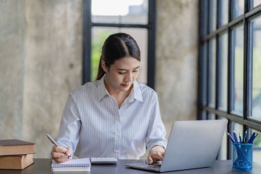 Asyalı iş kadını internet üzerinden ev ofisinden dizüstü bilgisayarla çalışıyor. Postaları kontrol ediyor ya da dairesinde yerde oturmuş telekomünikasyon yaparken bilgi arıyor.