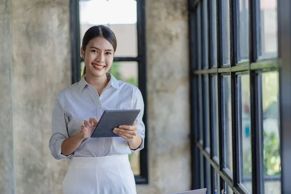 asian girl company employee smiling and holding a digital tablet Standing by the window in her office. Close-up. Financial accounting concept.