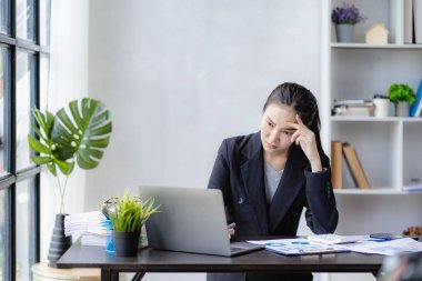 Asyalı iş kadını başını iş yerinde çok fazla evrak işi ve finansal muhasebe kavramı yüzünden tutuyor.