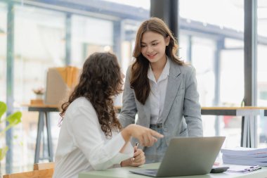 Konferans masasında dizüstü bilgisayarla çalışan iki neşeli iş kadını ve ofiste çalışma evrakları. Gayrimenkul projesini görüşmek üzere iş arkadaşları