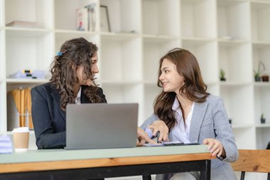 Konferans masasında dizüstü bilgisayarla çalışan iki neşeli iş kadını ve ofiste çalışma evrakları. Gayrimenkul projesini görüşmek üzere iş arkadaşları