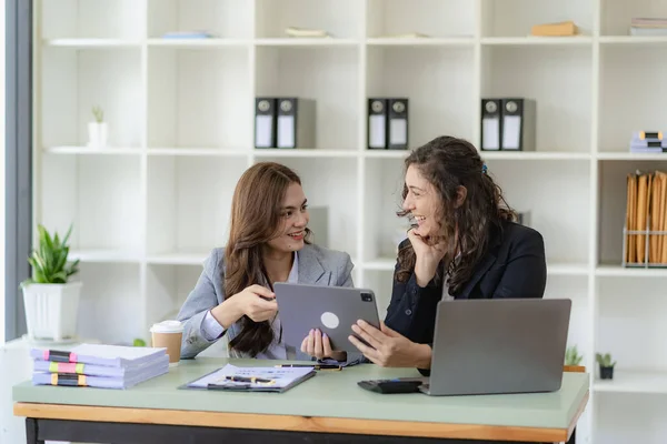 stock image Two young cheerful businesswoman working using digital tablet at conference table with work papers at office. Female business colleague using touch screen computer for real estate project discussion