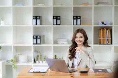 Bilgisayarda çalışan ve evrak işleri yapan kadın muhasebeci, vergi, döviz, muhasebe ve kameraya bakan mali danışman.