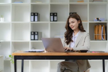 Bilgisayarda çalışan ve evrak işleri yapan kadın muhasebeci, vergi, döviz, muhasebe ve kameraya bakan mali danışman.