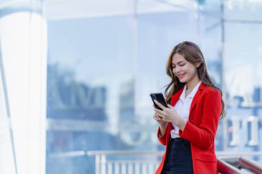 Açık havada elinde akıllı telefon tutan kırmızı elbiseli zarif gülümseyen kadının portresi. Arkadaşlarıyla sohbet etmek ve mesajlaşmak için cep telefonu kullanan neşeli bir kadın..