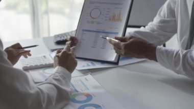İstatistiksel analiz planlama toplantısında beyin fırtınası yapan Asyalı işadamı ve takım lideri grafikleri gösteriyor ve mali başarı istatistikleri hakkında notlar alıyor. 4k 30p video.