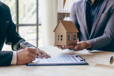 Emlakçılar konut satın almak ya da kiralamak için sözleşme teklif ediyorlar. Küçük bir bina modeline dokunan bir işadamı ve emlak sigortası resimleri kapatır