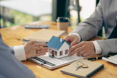 Emlakçılar konut satın almak ya da kiralamak için sözleşme teklif ediyorlar. Küçük bir bina modeline dokunan bir işadamı ve emlak sigortası resimleri kapatır