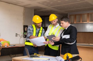 İnşaat sahasında mimari projesiyle veri çalışması ve tablet dizüstü bilgisayarı tartışan üç meslektaşımız mimari proje mühendisi için mimari planlar üzerinde çalışıyor.