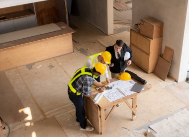 İnşaat sahasında mimari projesiyle veri çalışması ve tablet dizüstü bilgisayarı tartışan üç meslektaşımız mimari proje mühendisi için mimari planlar üzerinde çalışıyor.