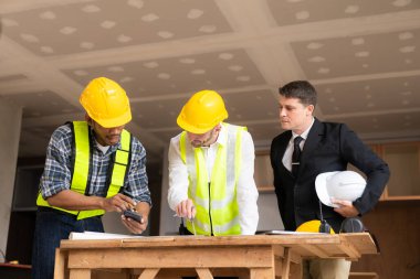 İnşaat sahasında mimari projesiyle veri çalışması ve tablet dizüstü bilgisayarı tartışan üç meslektaşımız mimari proje mühendisi için mimari planlar üzerinde çalışıyor.