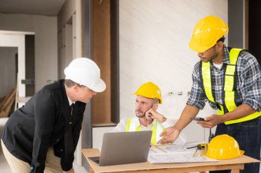 İnşaat sahasında mimari projesiyle veri çalışması ve tablet dizüstü bilgisayarı tartışan üç meslektaşımız mimari proje mühendisi için mimari planlar üzerinde çalışıyor.