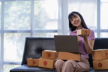Küçük bir işletme kurmak KOBİ işletme sahipleri, Asyalı kadın girişimciler kanepe üzerinde çalışma kutusu ve akıllı telefon dizüstü bilgisayarı müşterilere satılacak paketleme kutularını hazırlamak için çevrimiçi siparişler.