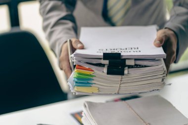 Asyalı ofis çalışanı masasında oturmuş ofisteki masadaki bir sürü kağıdı temizliyor.