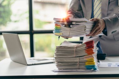 Asyalı ofis çalışanı masasında oturmuş ofisteki masadaki bir sürü kağıdı temizliyor.