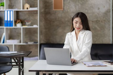 Asyalı iş kadını oturma odasında oturmuş evde bilgisayarla online toplantı yapıyor, finans dünyası kavramını kullanıyor..