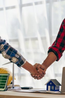 Yenilenebilir enerji konsepti müteahhitlik bürosunda yeni proje sözleşmesi planına başlamak için inşaat ekibi tokalaşması olan masa ve ev modeli güneş rüzgâr değirmeni üzerindeki sarı başlık