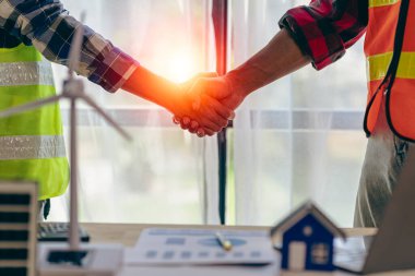 Yenilenebilir enerji konsepti müteahhitlik bürosunda yeni proje sözleşmesi planına başlamak için inşaat ekibi tokalaşması olan masa ve ev modeli güneş rüzgâr değirmeni üzerindeki sarı başlık