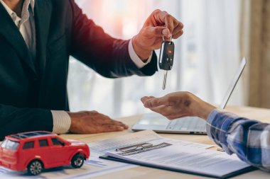 Terfiyi ve araba sigortasını açıkla. Bir araba satıcısı ya da satış müdürü araba sahibine anahtarları verir ve ofisteki bir masada araba sözleşmesinin şartlarını açıklar..