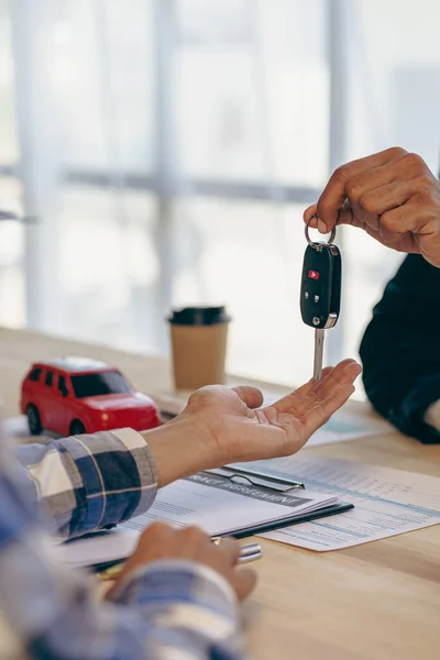 レンタルまたは購入のためのプロモーションと自動車保険を説明します 自動車販売業者又は販売管理者は 自動車の所有者に鍵を渡し 事務所の机における自動車契約の条件を説明する — ストック写真