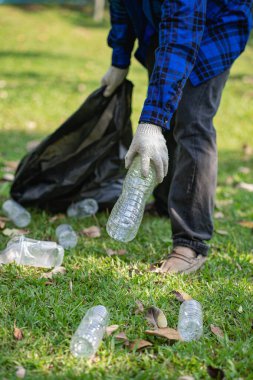 Close up of hands with plastic bottles with volunteer young man collecting plastic bottles in garbage bags on bench floor, earth day ecology concept cleaning
