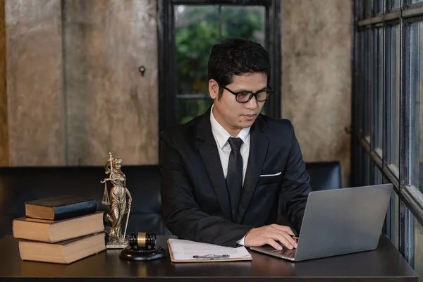 Asian young lawyer working with laptop and hammer with scales giving online legal advice explaining contract rules to legal advisor and justice office concept