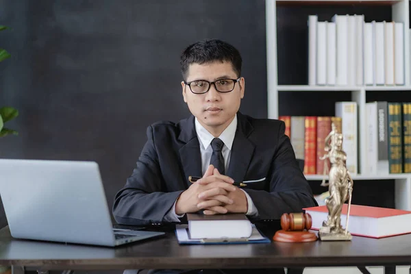 Asian young lawyer working with laptop and hammer with scales giving online legal advice explaining contract rules to legal advisor and justice office concept