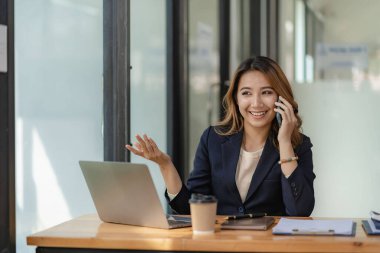 Ciddi Asyalı iş kadını müşteri hizmetlerini kullanarak masada oturuyor, satış müdürü ofisteki müşteriyle iş görüşmesi yapan bir kadına odaklanmış durumda.