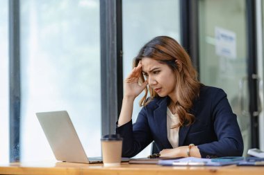 Stresli ve sinirli Asyalı muhasebeci masasında oturmuş ciddi iş kararları veriyor üzerinde çalıştığı proje için endişeleniyor ve ekrandaki acıya bakıyor.?