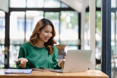 Bir kafede çalışan genç bir kadın dizüstü bilgisayar kullanıyor ve kahve içiyor. Uzaktan öğrenim için bilgisayar kullanıyor. Dükkandaki bir bankta oturuyor.