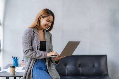 Dizüstü bilgisayarı olan genç bir kadın iş yerinde internet üzerinden iş arkadaşları ve müşterilerle iletişim kuruyor.