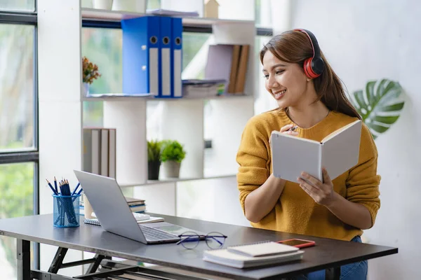 stock image Young asian student in headphones and looking at camera in future self education or learning concept, young girl student studying online at home with book and laptop