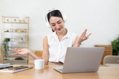 Kulaklıklı güzel Asyalı kız bilgisayarında ve cep telefonunda müzik dinliyor. Tatil boyunca iş yerinde müzik dinlemenin, ev konseptinin keyfini çıkarın..