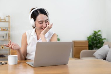 Kulaklıklı güzel Asyalı kız bilgisayarında ve cep telefonunda müzik dinliyor. Tatil boyunca iş yerinde müzik dinlemenin, ev konseptinin keyfini çıkarın..