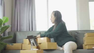 Olgun bir kadın iş kuruyor, KOBİ sahibi, bayan girişimci çalışıyor ve evdeki tablet dizüstü bilgisayarla online siparişi kontrol ediyor. KME iş konsepti çevrimiçi paket teslimatı 4k