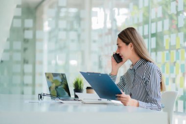 Oldukça başarılı Asyalı iş kadını akıllı telefon kullanıyor ve masa başında çalışırken aylık hesapları kontrol ediyor ve şirkette harcama yapıyor.
