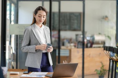 Parlak modern ofisindeki tablet bilgisayarında çalışan gülümseyen Asyalı iş kadını grafik belgeleriyle finansal rapor harcamalarını hesaplıyor.