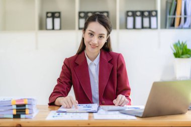 Parlak modern ofisindeki tablet bilgisayarında çalışan gülümseyen Asyalı iş kadını grafik belgeleriyle finansal rapor harcamalarını hesaplıyor.