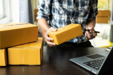Küçük işletme sahibi KOBİ kuruyor. Asyalı adam online siparişleri kontrol ediyor, ürünleri satıyor, kutularla çalışıyor. Ev ofisi serbest çalışma çevrimiçi iş teslimatı konsepti