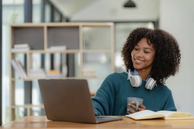 Kulaklık takan genç bir kız öğrenci çevrimiçi video iletişimi eğitimi alıyor mutlu kız öğrenci bilgisayar ekranına bakıyor, webinars izliyor ya da kütüphanede webcam 'de görüntülü sohbet yapıyor..