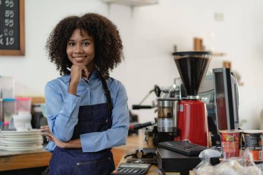 Barista, kahve dükkanı açılışı, Afrikalı Amerikalı bayan girişimci tezgahın önünde duruyor. Önlüklü genç bir bayan garson mağazada müşterilere servis yapıyor.