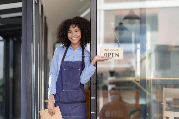 Barista Startup Coffee Shop Entrepreneur African American Woman Standing at the Door of a Casual Coffee Shop Showing an Open Sign Happy and cheerful smile with service, food and drink concept