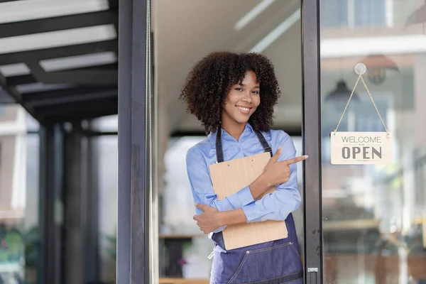 Barista Startup Coffee Shop Entrepreneur African American Woman Standing at the Door of a Casual Coffee Shop Showing an Open Sign Happy and cheerful smile with service, food and drink concept