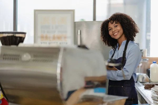 Barista, coffee shop startup, African American female entrepreneur standing in front of the counter. A young female waitress in an apron serving customers in a store