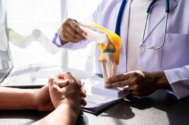 Doktorun muayenesi sırasında diz modelini erkek hastaya gösteren fizyoterapist.