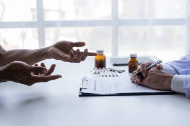 Beyaz üniformalı erkek doktor erkek hastayla sonuçları ya da belirtileri tartışıyor ya da doktorlar hastalara hastanedeki ilaçlarla ilgili tavsiyelerde bulunuyor..