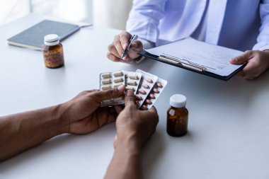 Beyaz üniformalı erkek doktor erkek hastayla sonuçları ya da belirtileri tartışıyor ya da doktorlar hastalara hastanedeki ilaçlarla ilgili tavsiyelerde bulunuyor..