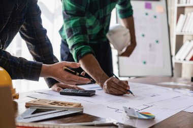 Planı işaret eden mühendis ve dizüstü bilgisayar kullanarak proje tasarım mimarı İnşaat Müteahhiti ve inşaat projesinin kat planlama projesiyle ilgili toplantı düzenliyor.